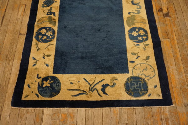 Dark blue rug with a wide tan border featuring medallions and florals on distressed wood flooring.