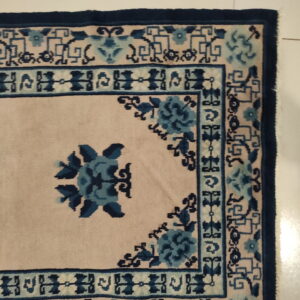 Blue and beige rug featuring floral motifs and a complex geometric border on a light tiled floor.