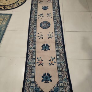 Low-pile cream and blue runner rug with floral medallions and geometric borders on light tile flooring.
