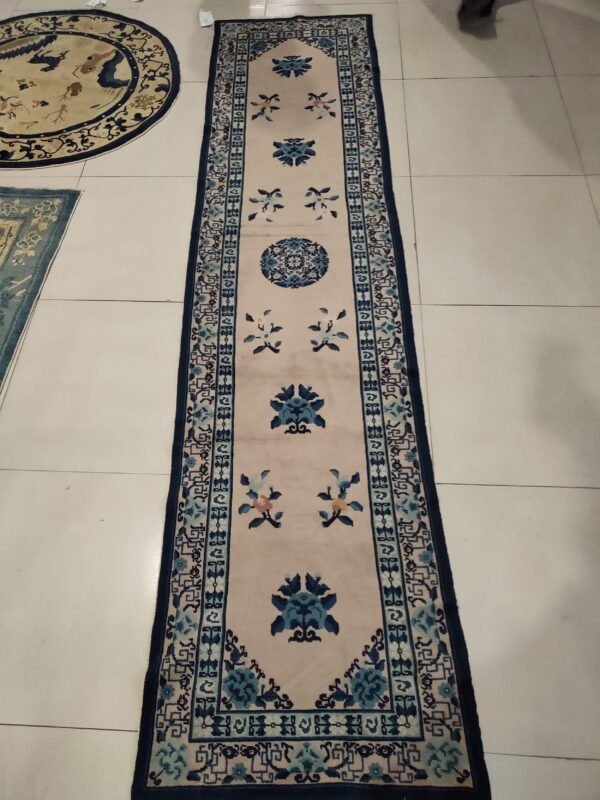 Low-pile cream and blue runner rug with floral medallions and geometric borders on light tile flooring.