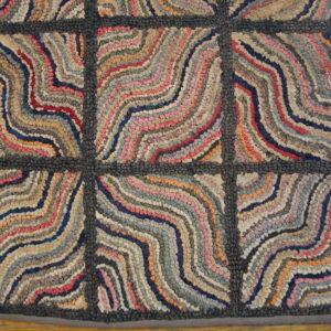 Textured rug with a dark gray grid pattern contains wavy bands of multicolored red, blue, and tan fabric strips.