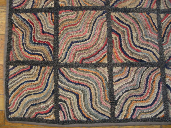 Textured rug with a dark gray grid pattern contains wavy bands of multicolored red, blue, and tan fabric strips.