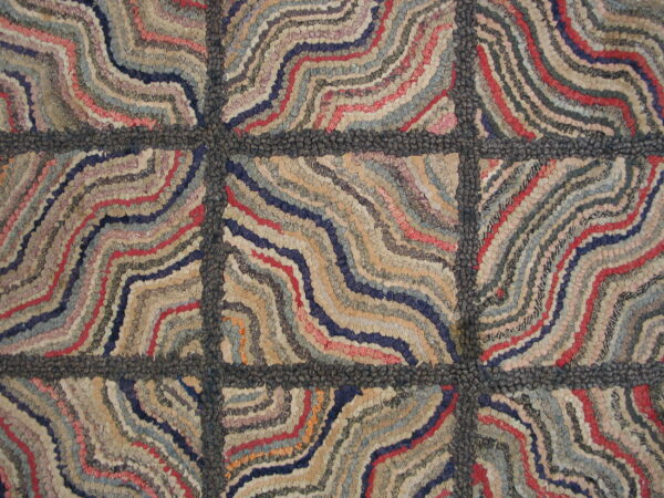 A close-up of a hooked rug featuring wavy, colorful stripes within a dark gray block pattern.