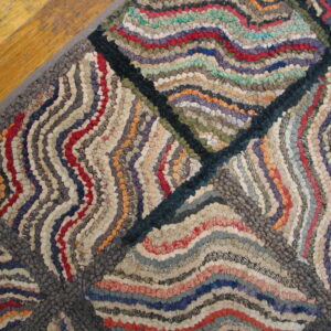 Multicolor hooked rug featuring wavy stripes inside geometric quadrants rests on a distressed wooden floor.