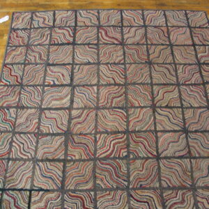Textured rug with a dark grid pattern and multicolored wavy lines sits on hardwood flooring.