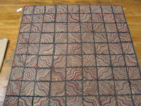 Textured rug with a dark grid pattern and multicolored wavy lines sits on hardwood flooring.