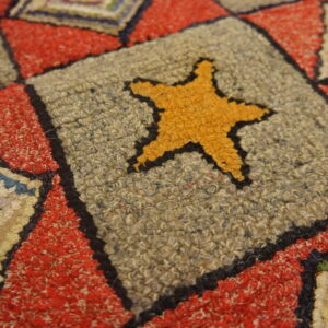 Textured rug detail shows a yellow star on a gray square, bordered by speckled red and multicolored stripes.