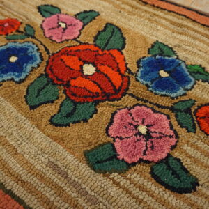 Highly textured rug displaying large red, blue, and pink floral designs on a tan looped background.