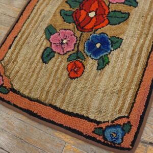 Hooked rug with floral pattern in red, pink, and blue on a beige striped background and orange border.