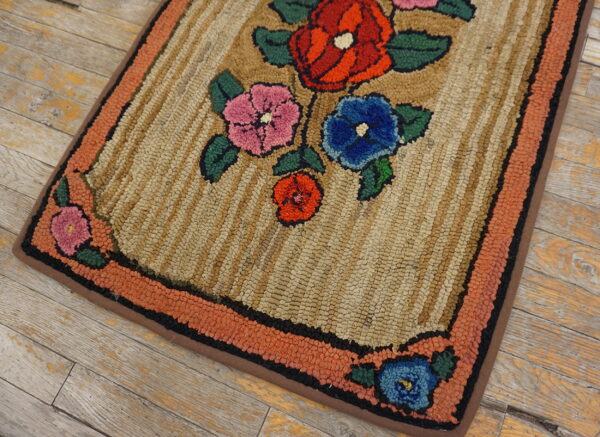 Hooked rug with floral pattern in red, pink, and blue on a beige striped background and orange border.
