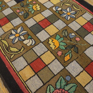Textured, multicolored rug featuring bold floral motifs over a diagonal checkerboard pattern on wood flooring.
