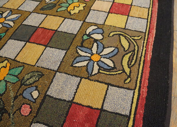 Textured rug detail showing colorful floral patterns superimposed over a checkered grid on hardwood floor.