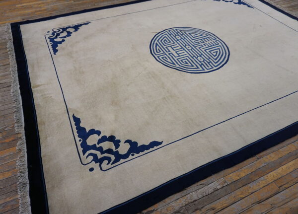 Light-colored rug with a blue central medallion and corner scrolls rests on rustic wood plank flooring.