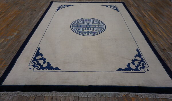 Light beige rug featuring a dark blue geometric medallion and stylized cloud spandrels on a rustic wood floor.