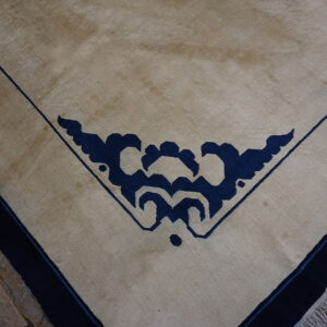 Tan low-pile rug with a dark blue corner motif and thin blue lines on visible wood planks.