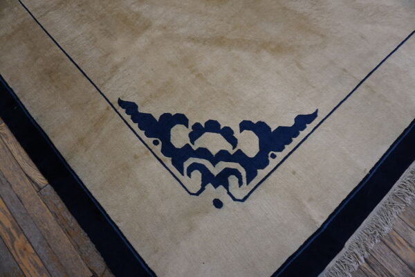 Tan low-pile rug with a dark blue corner motif and thin blue lines on visible wood planks.