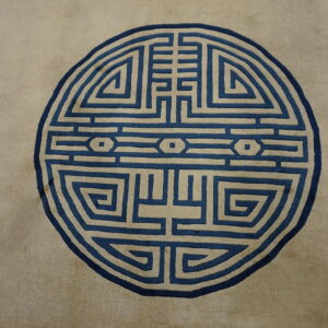 Muted tan rug featuring a prominent round maze-like medallion pattern in deep blue and cream.