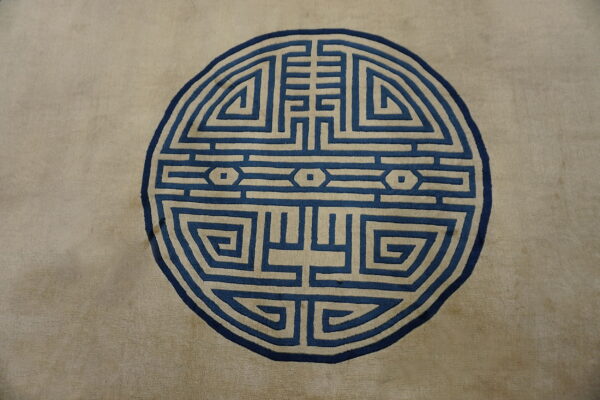 Muted tan rug featuring a prominent round maze-like medallion pattern in deep blue and cream.