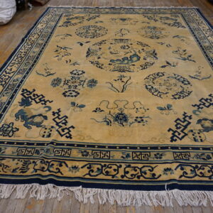 Low-pile gold rug with navy and light blue figural and geometric patterns rests on plank wood flooring.