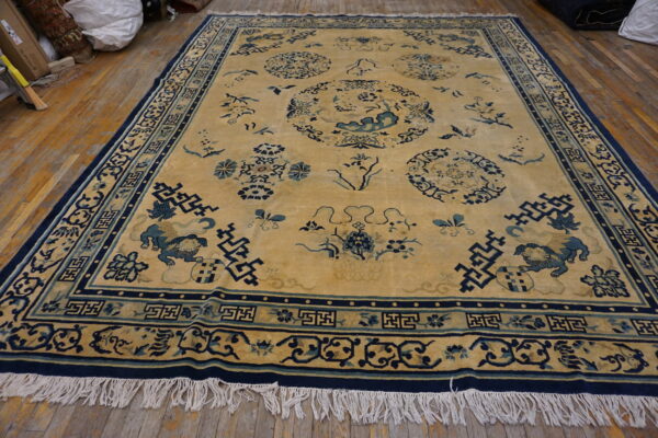 Low-pile gold rug with navy and light blue figural and geometric patterns rests on plank wood flooring.