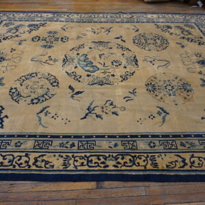 Tan and indigo blue low-pile rug featuring scattered oriental medallions and elaborate fretwork borders on wood flooring.