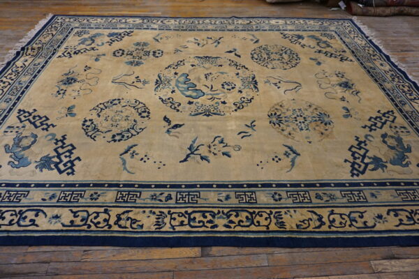 Tan and indigo blue low-pile rug featuring scattered oriental medallions and elaborate fretwork borders on wood flooring.