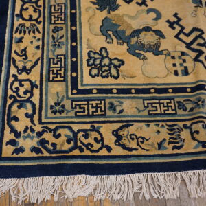 Detailed view of a gold and navy rug featuring lion and fretwork patterns on hardwood flooring.