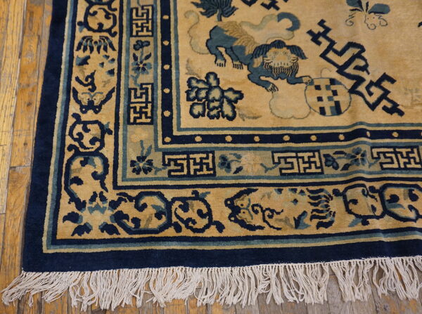 Detailed view of a gold and navy rug featuring lion and fretwork patterns on hardwood flooring.
