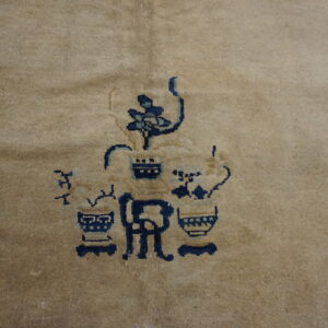 Detail of a muted camel rug with an indigo and light blue floral and vase motif.