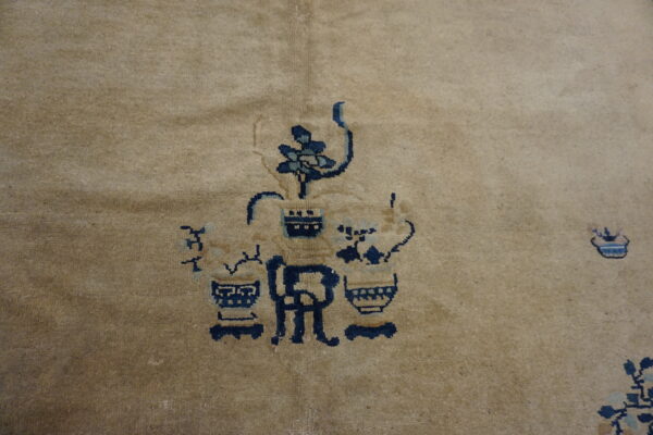 Detail of a muted camel rug with an indigo and light blue floral and vase motif.