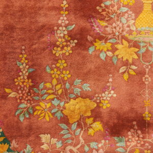 Detailed close-up of a rust-colored rug featuring yellow and pink floral motifs and a deep green edge panel.