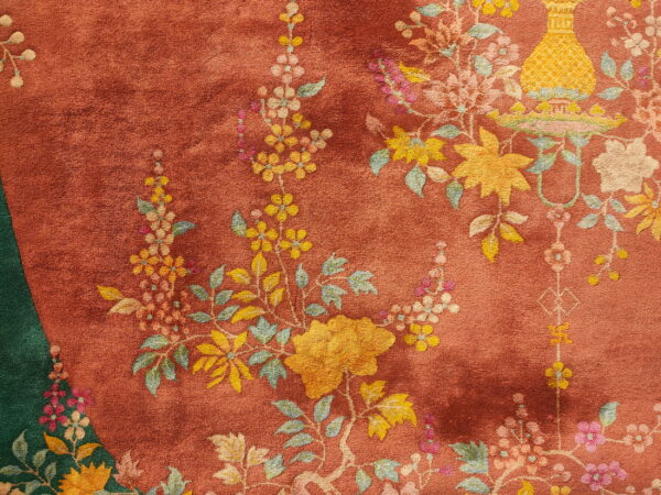 Detailed close-up of a rust-colored rug featuring yellow and pink floral motifs and a deep green edge panel.