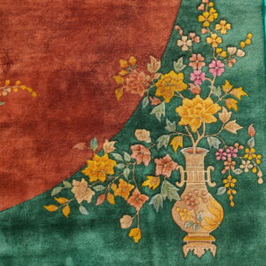 Rust and green rug detail showing a carved floral design with a central beige vase motif.