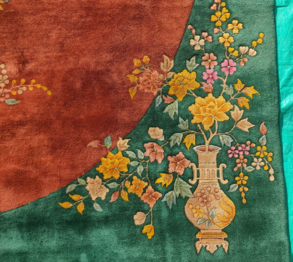 Rust and green rug detail showing a carved floral design with a central beige vase motif.