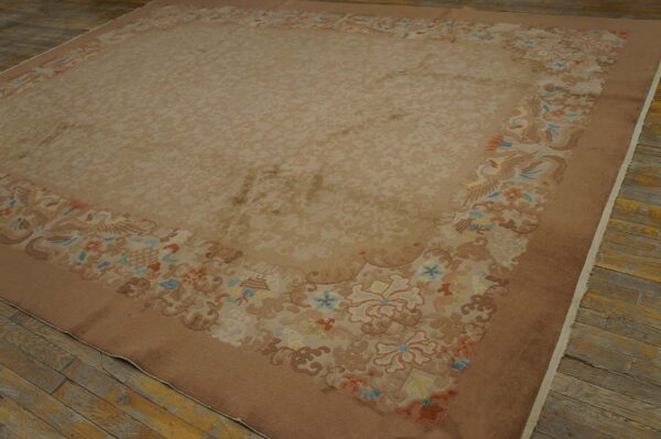 Large beige rug with a subtle field pattern and a brown border featuring multicolored floral and avian designs.