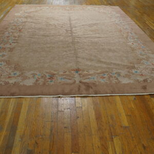Mauve rug with faded floral and bird border designs lays on distressed wooden plank flooring.