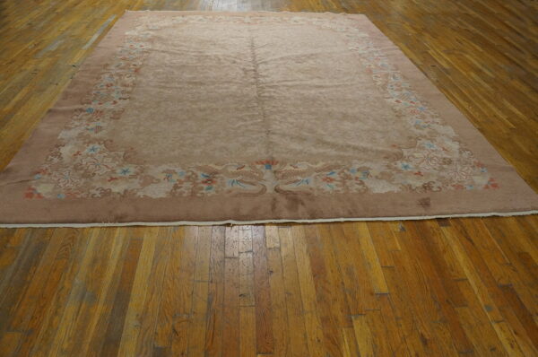 Mauve rug with faded floral and bird border designs lays on distressed wooden plank flooring.