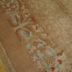 Taupe rug detail showing a colorful bird and floral border next to aged yellow wood floors.