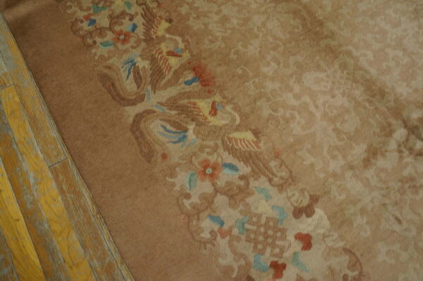 Taupe rug detail showing a colorful bird and floral border next to aged yellow wood floors.