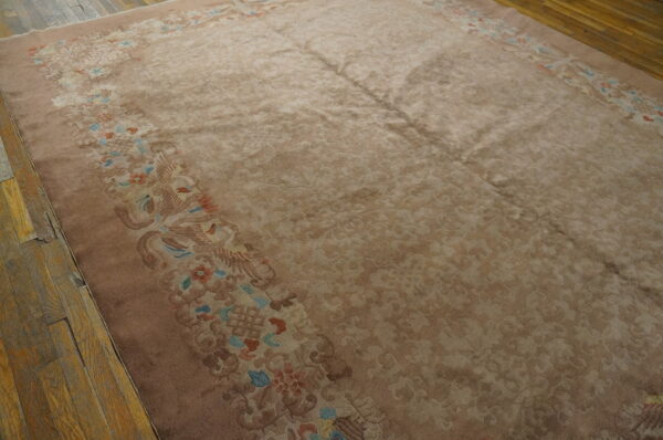 Taupe field rug with a detailed border in rose, blue, and coral on distressed wood flooring.