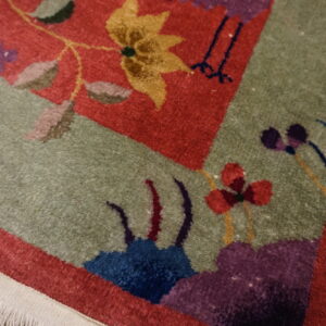 Close-up of a cut pile rug showing stylized red, sage, purple, and yellow floral patterns and fringe.