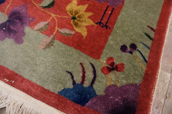 Close-up of a cut pile rug showing stylized red, sage, purple, and yellow floral patterns and fringe.