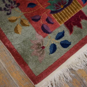 Medium pile green and red floral rug corner with purple, blue, and gold accents, fringed on wood planks.