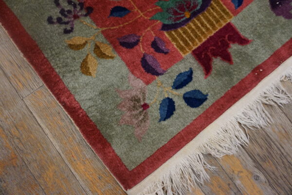 Medium pile green and red floral rug corner with purple, blue, and gold accents, fringed on wood planks.