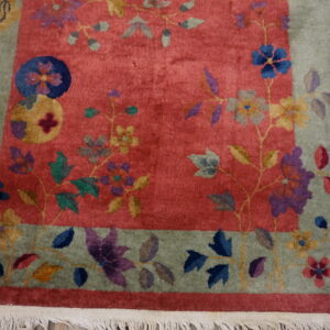 Coral rug with a sage floral border and bright multicolored blossoms lies on rustic wood flooring.