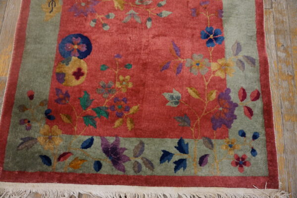 Coral rug with a sage floral border and bright multicolored blossoms lies on rustic wood flooring.