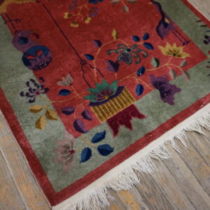 Red rug with colorful floral and bird patterns, a green border, and fringe on gray wood floors.