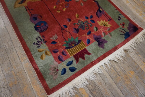 Red rug with colorful floral and bird patterns, a green border, and fringe on gray wood floors.