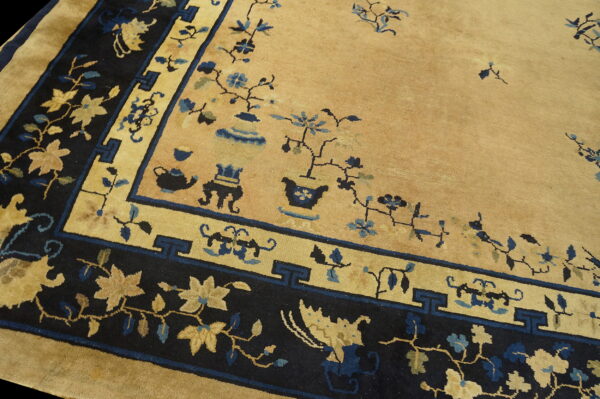 Golden tan rug with dark navy and blue borders, featuring sparse floral and vase motifs.