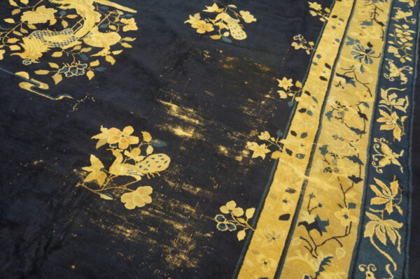 Worn dark blue rug featuring gold floral and avian designs bordered by wide yellow stripes.